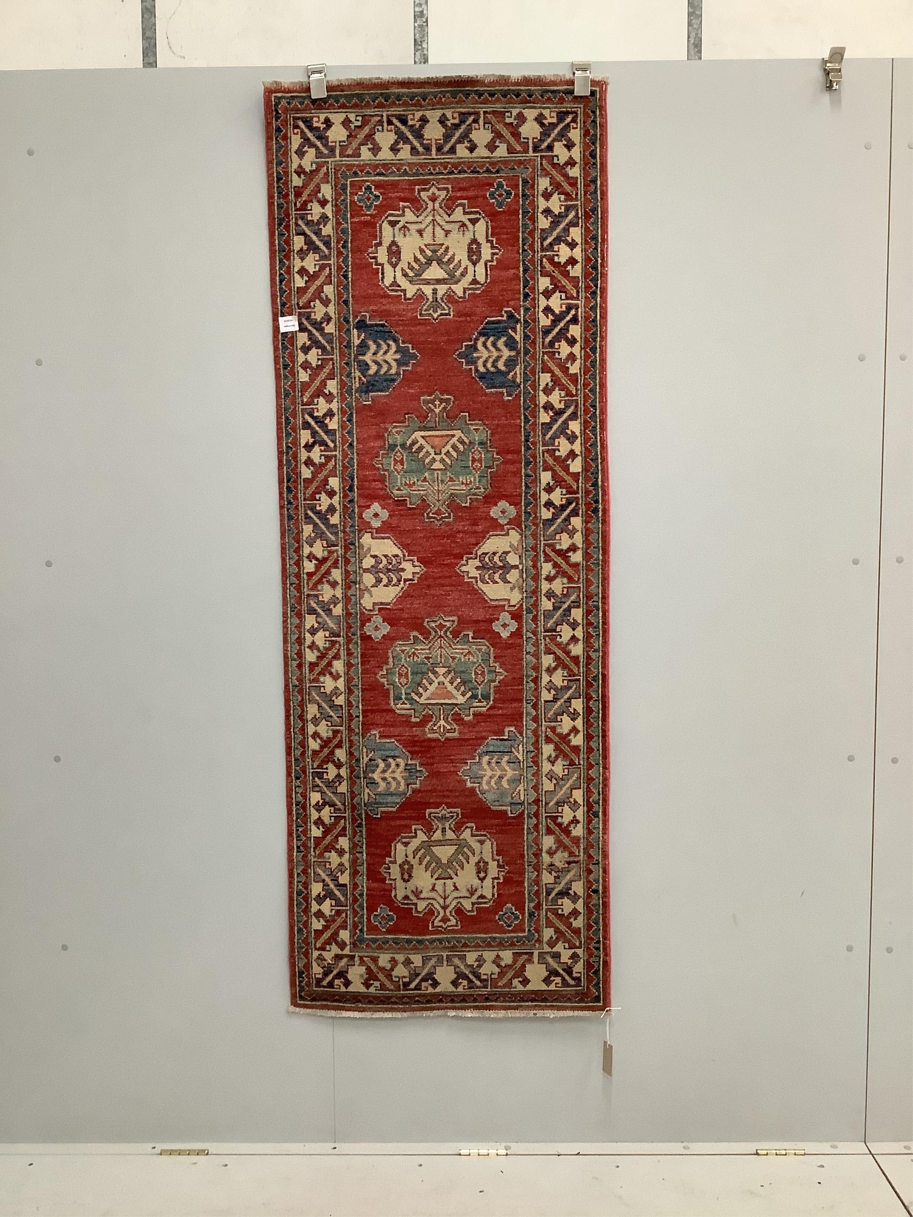 A Caucasian style brick red ground rug, 200 x 72cm. Condition - good